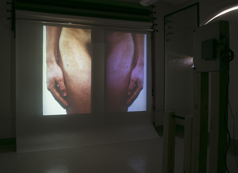 Installation image of Read featuring a projected image of the artist's body which is doubled and mirrored as it passes through a two way mirror.