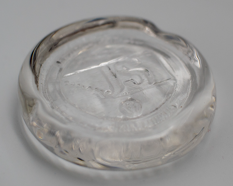 A disc of clear glass with a seal design stamped into its surface.