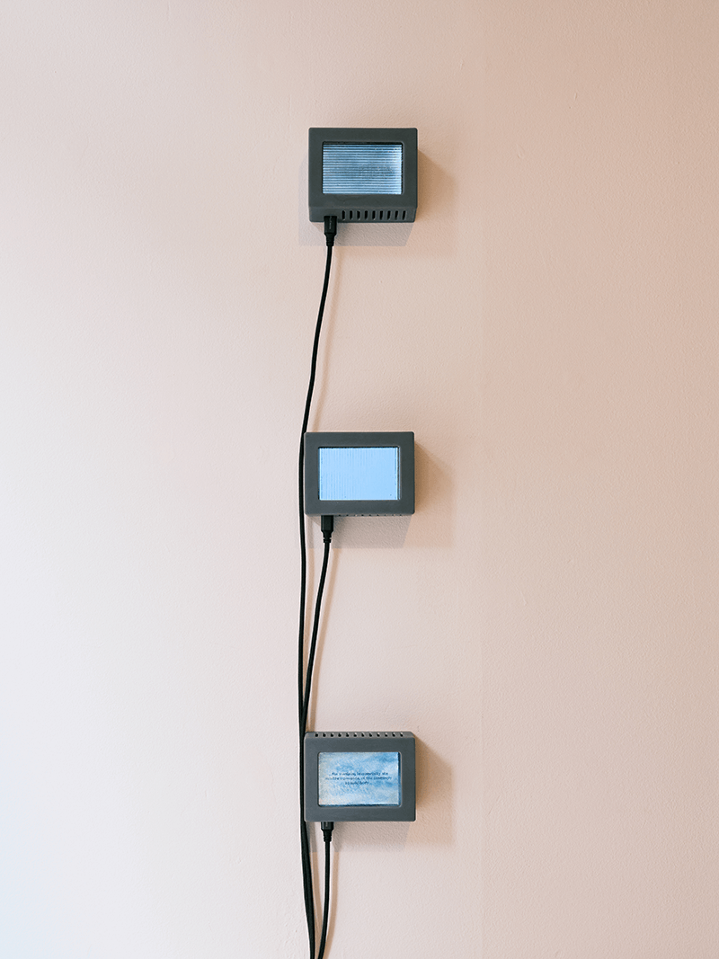 3 rectangular grey screen sculptures arranged vertically on a wall with black wires attached to each.