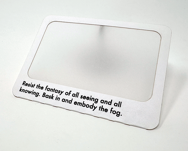 A white paper frame with a translucent paper interior. The bottom of the frame has black text which says 'Resist the fantasy of all seeing and all knowing. Bask in and embody the fog.'